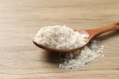 Photo of Fresh coconut flour in spoon on wooden table, closeup