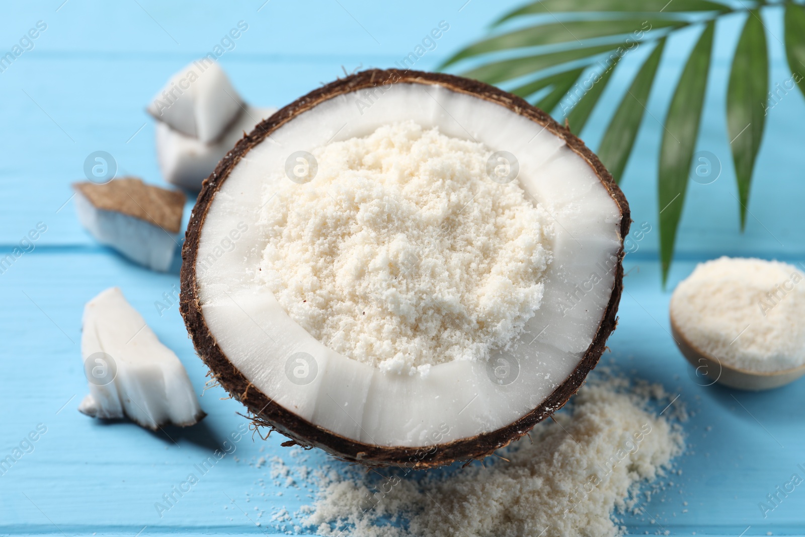 Photo of Fresh coconut flour, nuts and palm leaf on light blue wooden table