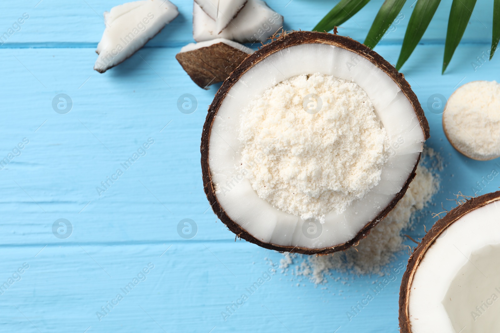 Photo of Fresh coconut flour, nuts and palm leaf on light blue wooden table, flat lay. Space for text