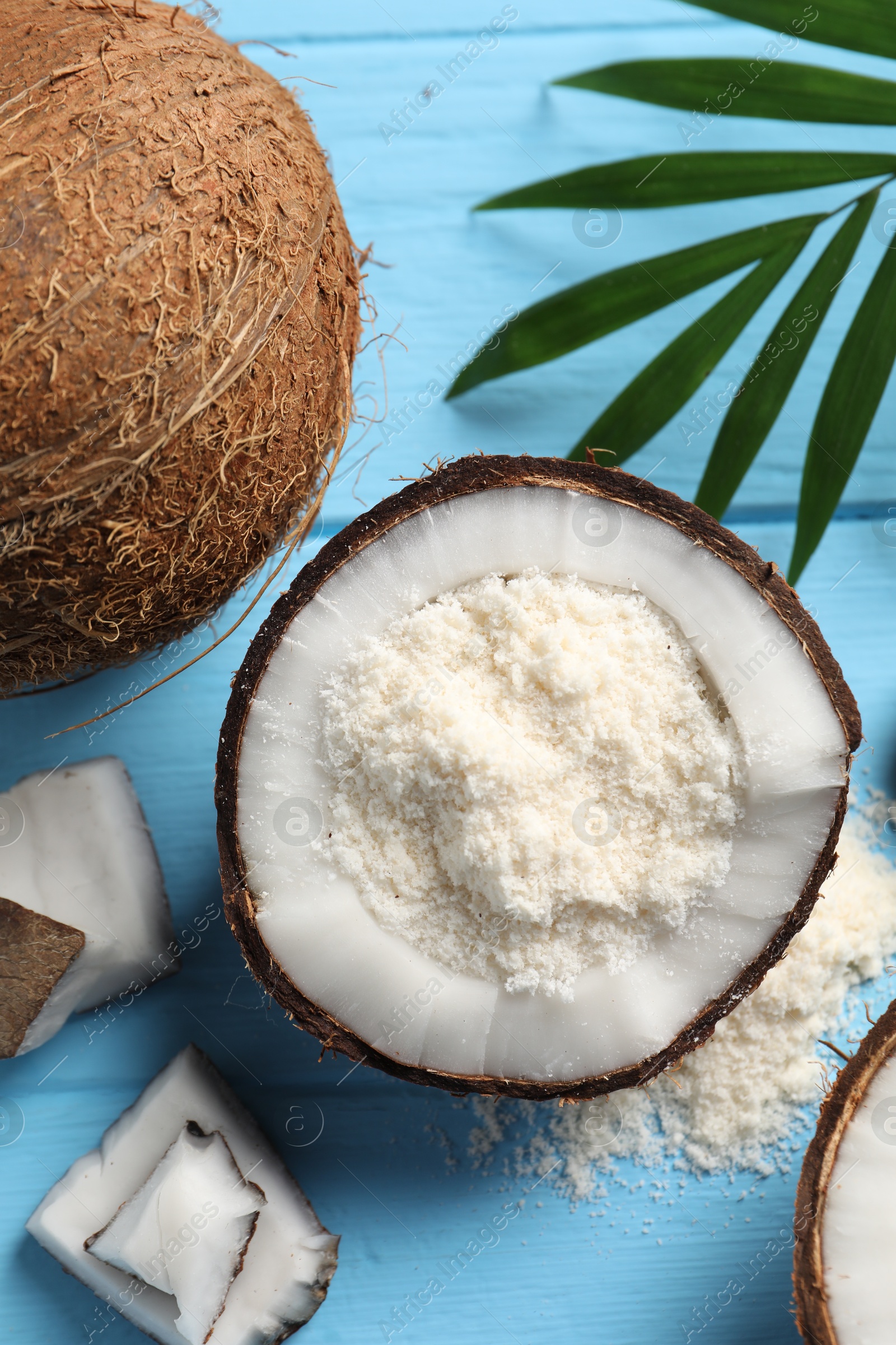 Photo of Fresh coconut flour, nuts and palm leaf on light blue wooden table, flat lay