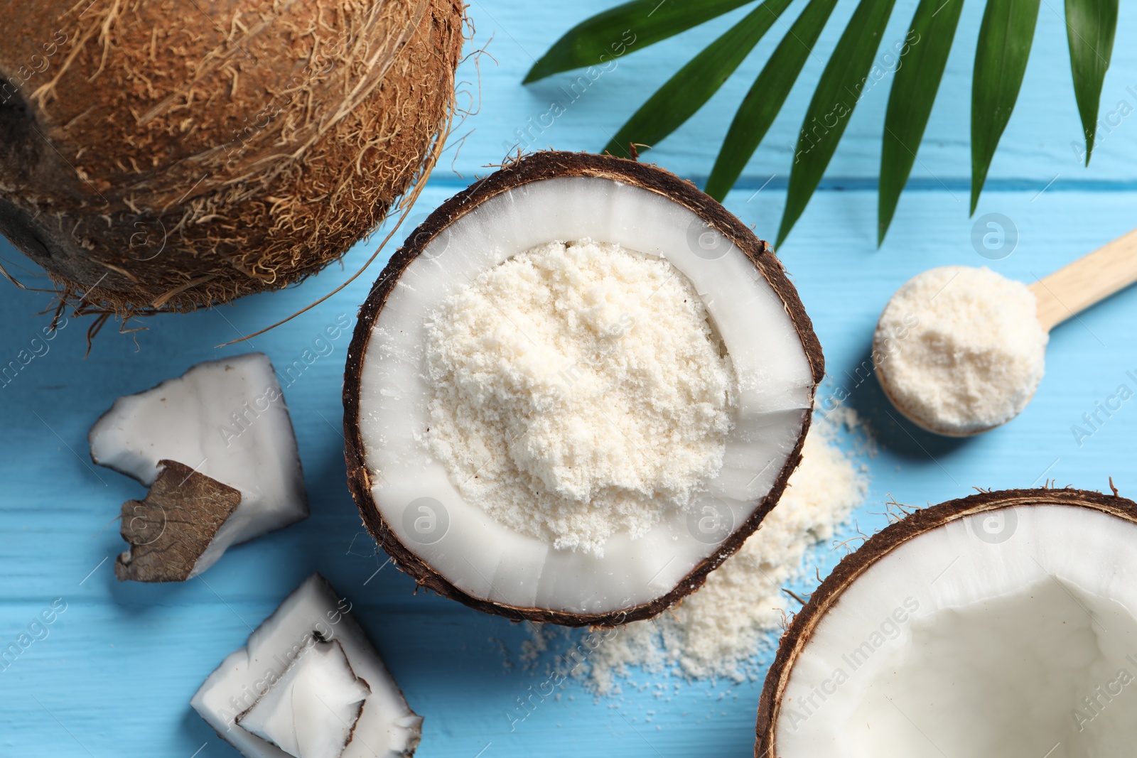 Photo of Fresh coconut flour, nuts, spoon and palm leaf on light blue wooden table, flat lay