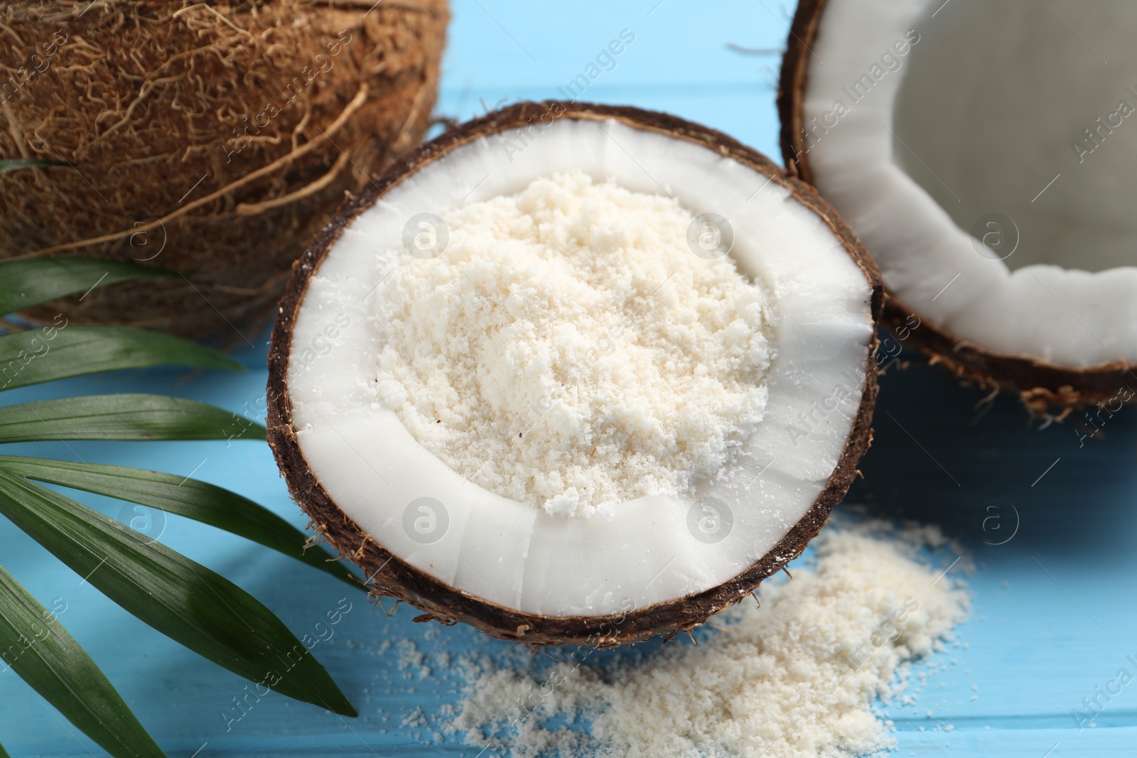 Photo of Fresh coconut flour, nuts and palm leaf on light blue wooden table