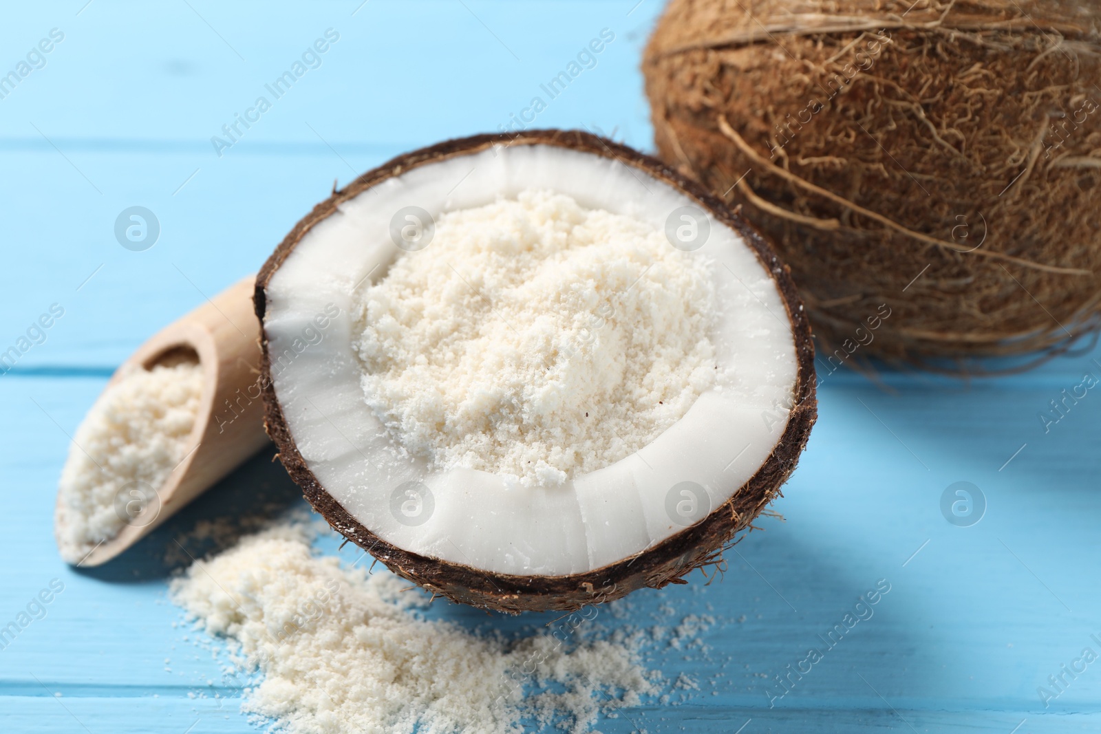 Photo of Fresh coconut flour in nut and scoop on light blue wooden table