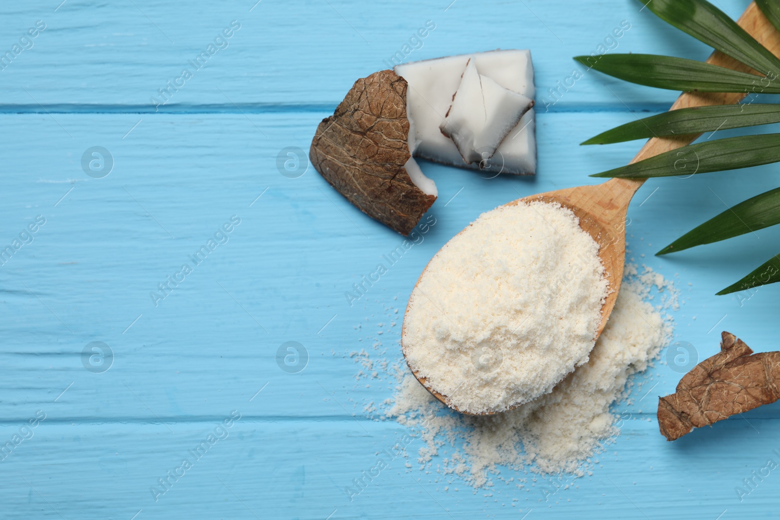 Photo of Fresh coconut flour in spoon, nut and palm leaf on light blue wooden table, flat lay. Space for text