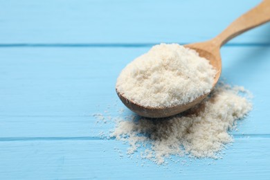 Photo of Fresh coconut flour in spoon on light blue wooden table, closeup. Space for text