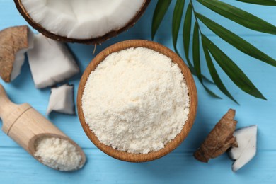 Photo of Fresh coconut flour in bowl, scoop, nut and palm leaf on light blue wooden table, flat lay