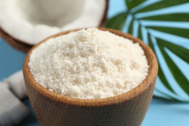 Photo of Fresh coconut flour in bowl, nut and palm leaf on light blue table, closeup