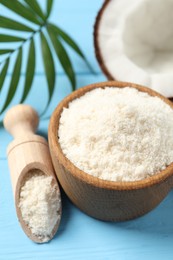 Photo of Fresh coconut flour in bowl, scoop, nut and palm leaf on light blue wooden table