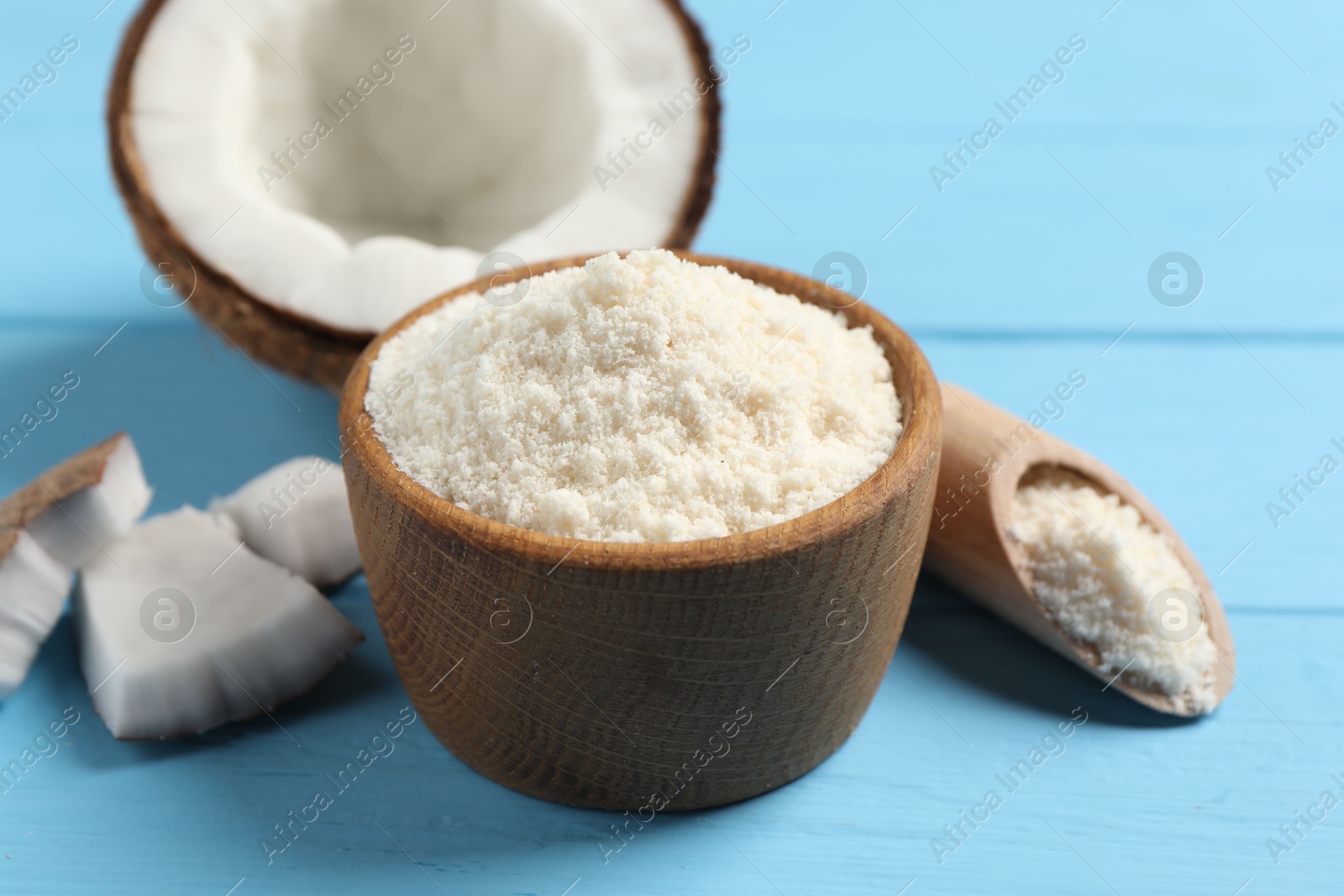 Photo of Fresh coconut flour in bowl, scoop and nut on light blue wooden table