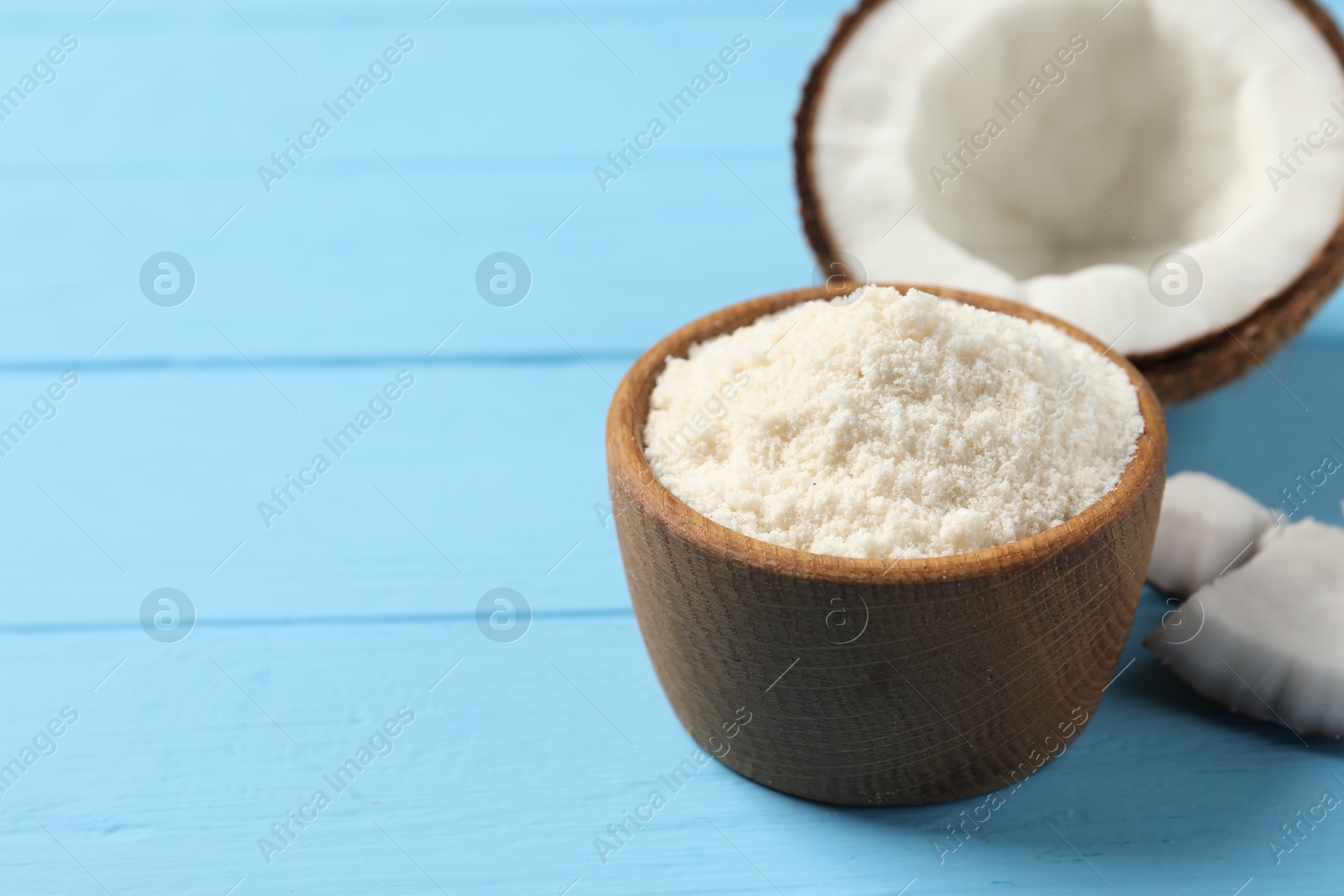 Photo of Fresh coconut flour in bowl and nut on light blue wooden table, space for text