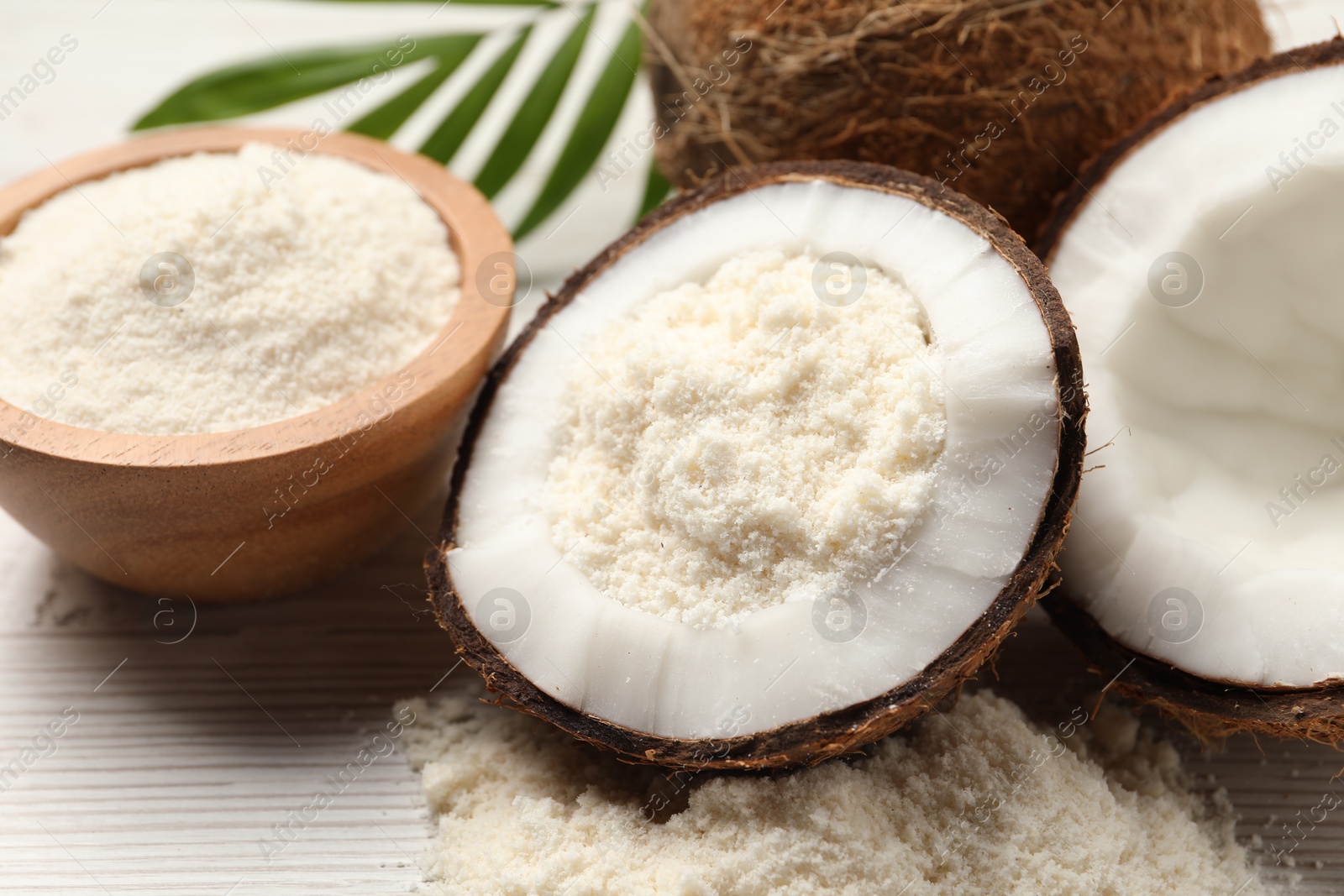 Photo of Fresh coconut flour, nuts, bowl and palm leaf on wooden table