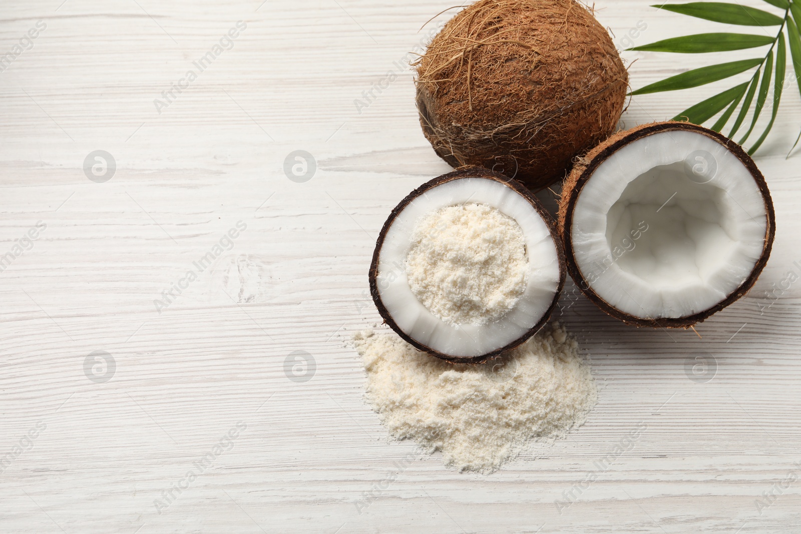 Photo of Fresh coconut flour, nuts and palm leaf on wooden table, space for text