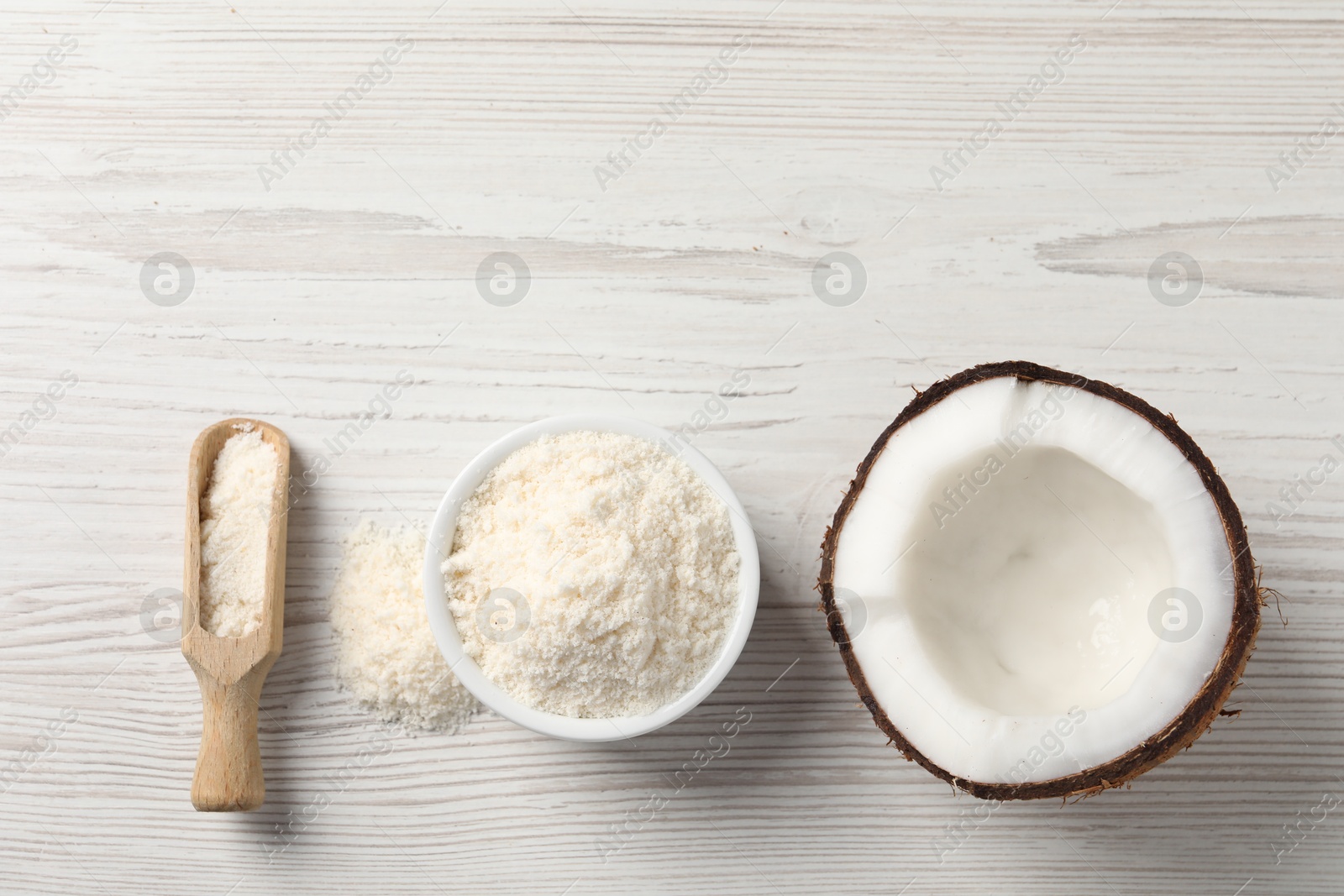 Photo of Fresh coconut flour in bowl, scoop and nut on white wooden table, flat lay