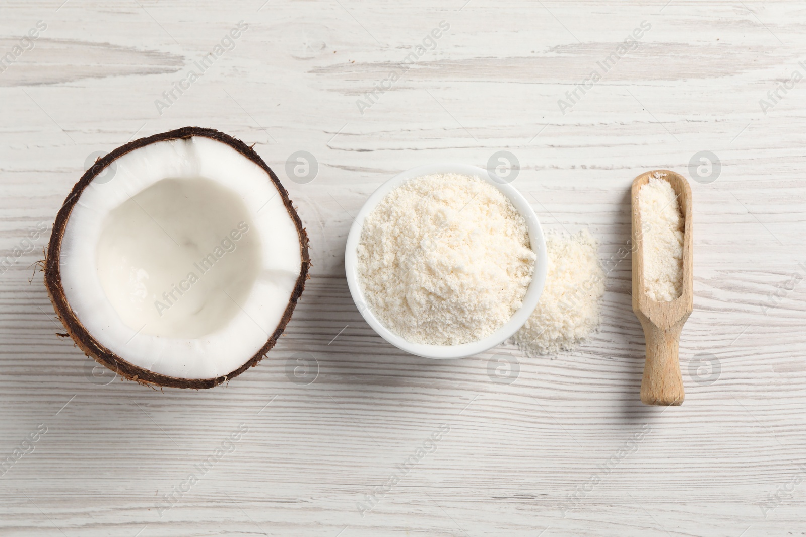 Photo of Fresh coconut flour in bowl, scoop and nut on white wooden table, flat lay