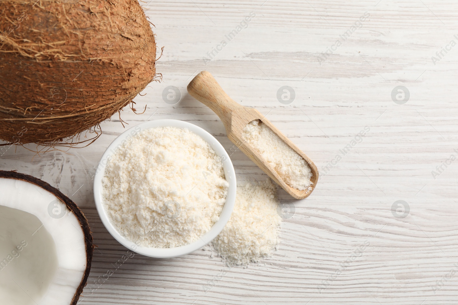 Photo of Fresh coconut flour in bowl, scoop and nuts on white wooden table, flat lay. Space for text