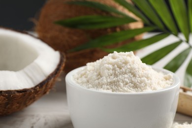 Photo of Fresh coconut flour in bowl, nuts and palm leaf on white table, closeup