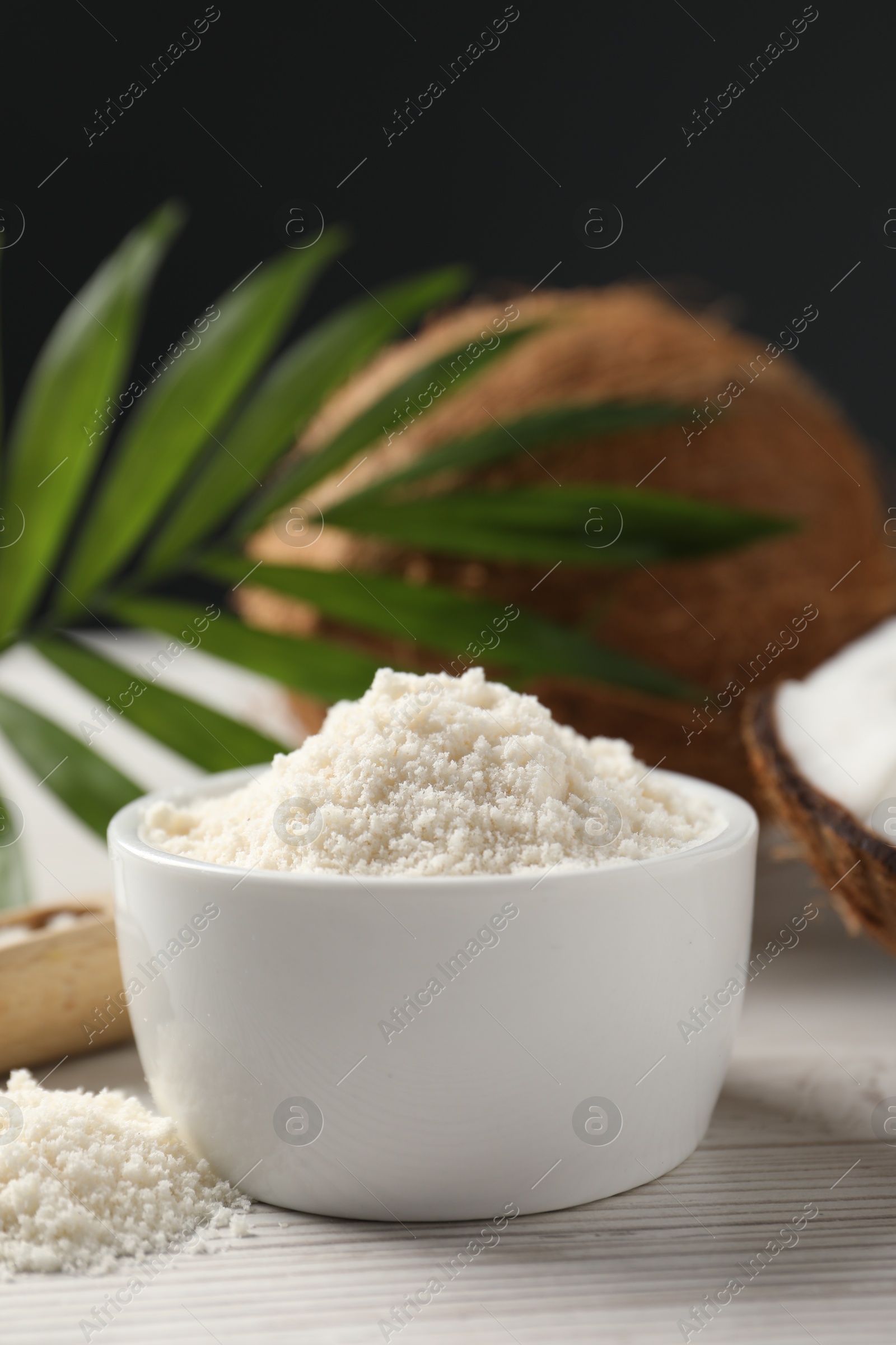 Photo of Fresh coconut flour in bowl, nut and palm leaf on white wooden table