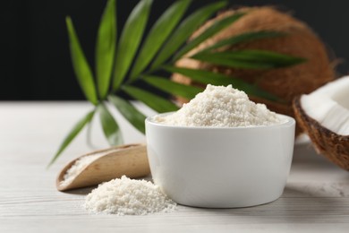 Photo of Fresh coconut flour in bowl, nuts, palm leaf and scoop on white wooden table