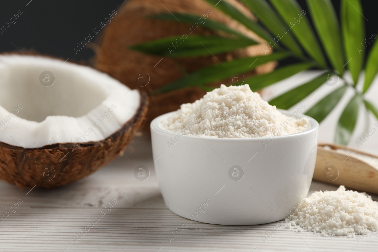 Photo of Fresh coconut flour in bowl, nuts and palm leaf on white wooden table