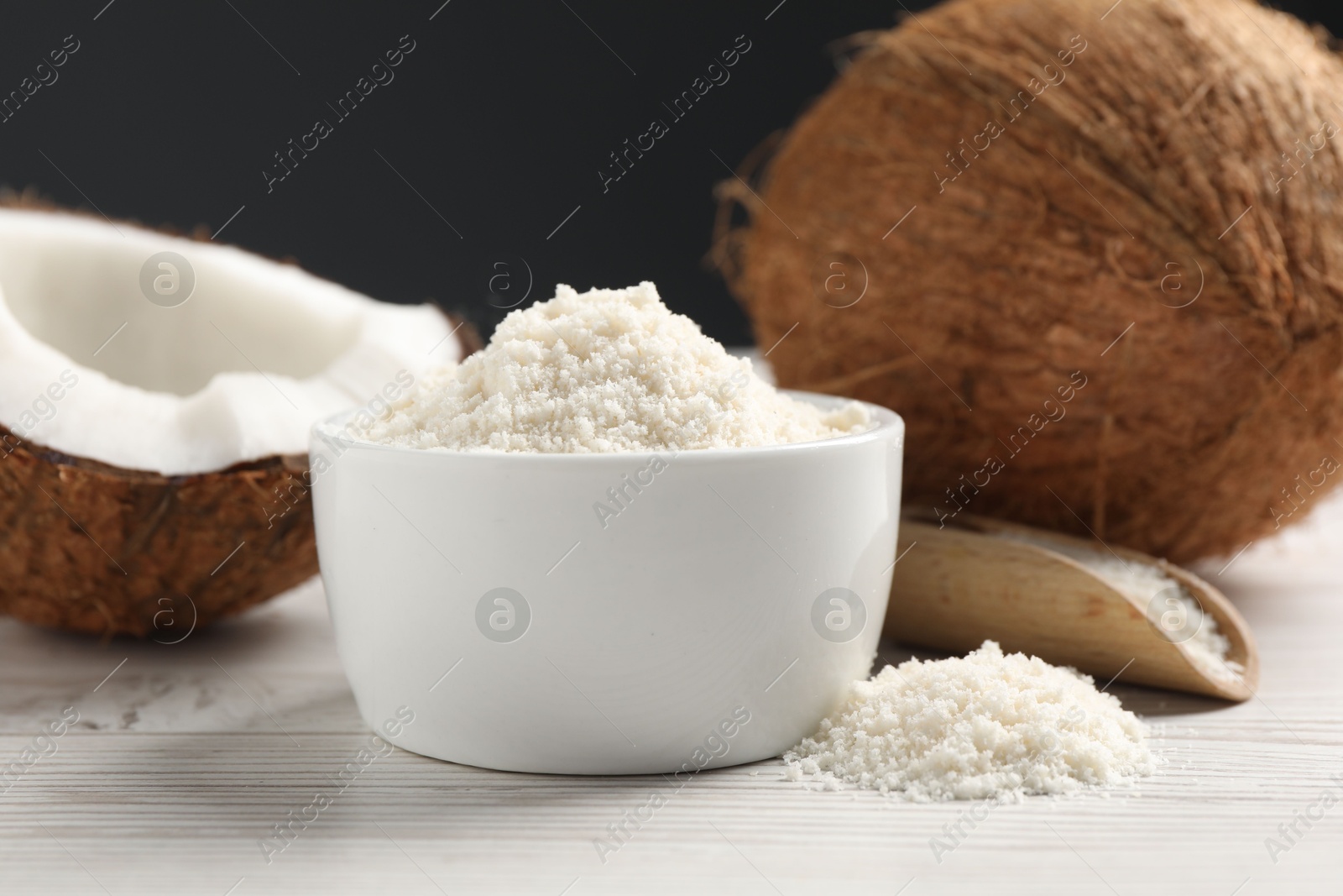 Photo of Fresh coconut flour in bowl, nuts and scoop on white wooden table