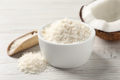 Photo of Fresh coconut flour in bowl, nut and scoop on white wooden table