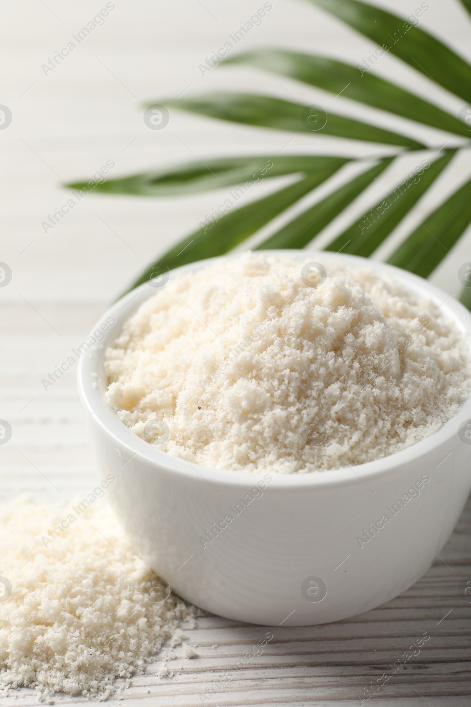 Photo of Fresh coconut flour in bowl and palm leaf on white wooden table