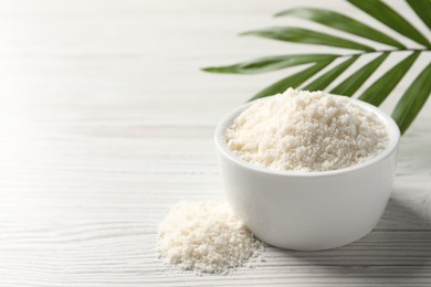 Photo of Fresh coconut flour in bowl and palm leaf on white wooden table, space for text