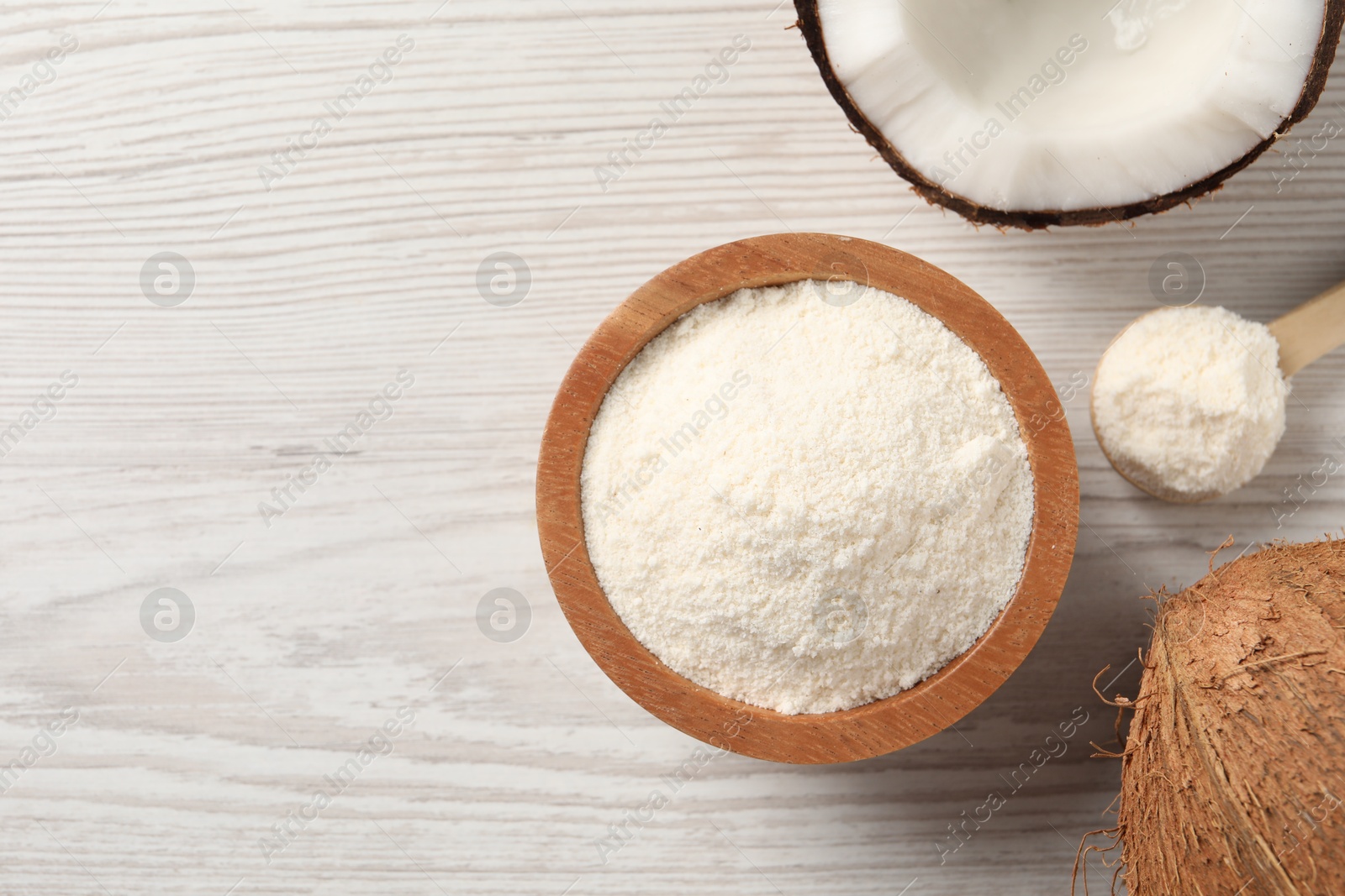 Photo of Fresh coconut flour in bowl, spoon and nut on white wooden table, flat lay. Space for text