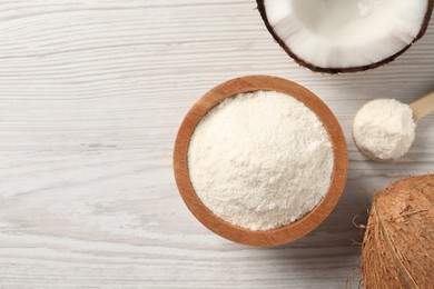 Fresh coconut flour in bowl, spoon and nut on white wooden table, flat lay. Space for text