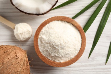 Photo of Fresh coconut flour in bowl, spoon, palm leaf and nut on white wooden table, flat lay