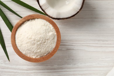 Photo of Fresh coconut flour in bowl, palm leaf and nut on white wooden table, flat lay. Space for text