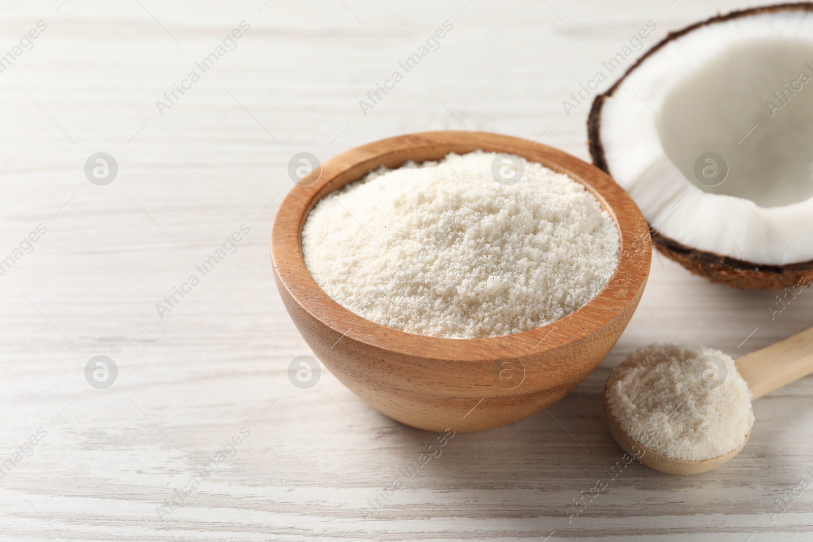 Photo of Fresh coconut flour in bowl, spoon and nut on white wooden table, space for text