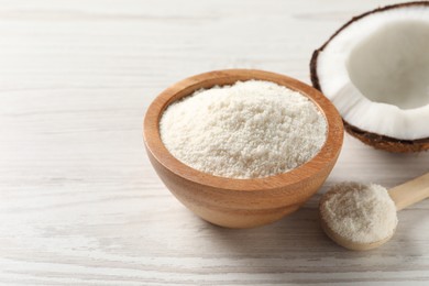 Photo of Fresh coconut flour in bowl, spoon and nut on white wooden table, space for text