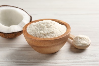 Photo of Fresh coconut flour in bowl, spoon and nut on white wooden table