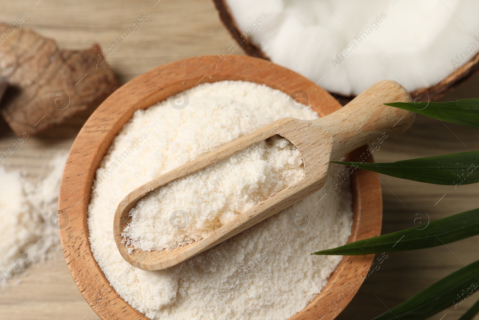 Photo of Fresh coconut flour in bowl, scoop, nut and palm leaf on wooden table, above view