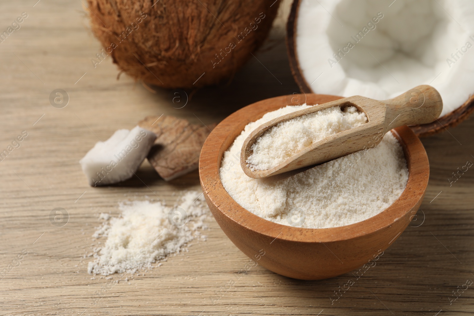 Photo of Fresh coconut flour in bowl, scoop and nut on wooden table