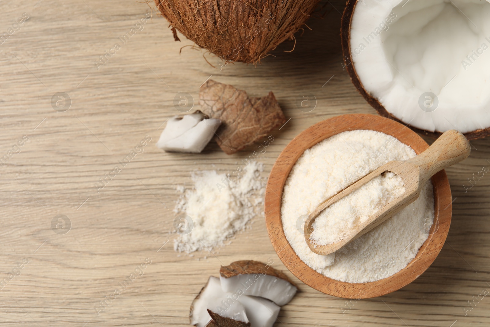 Photo of Fresh coconut flour in bowl, scoop and nut on wooden table, flat lay. Space for text