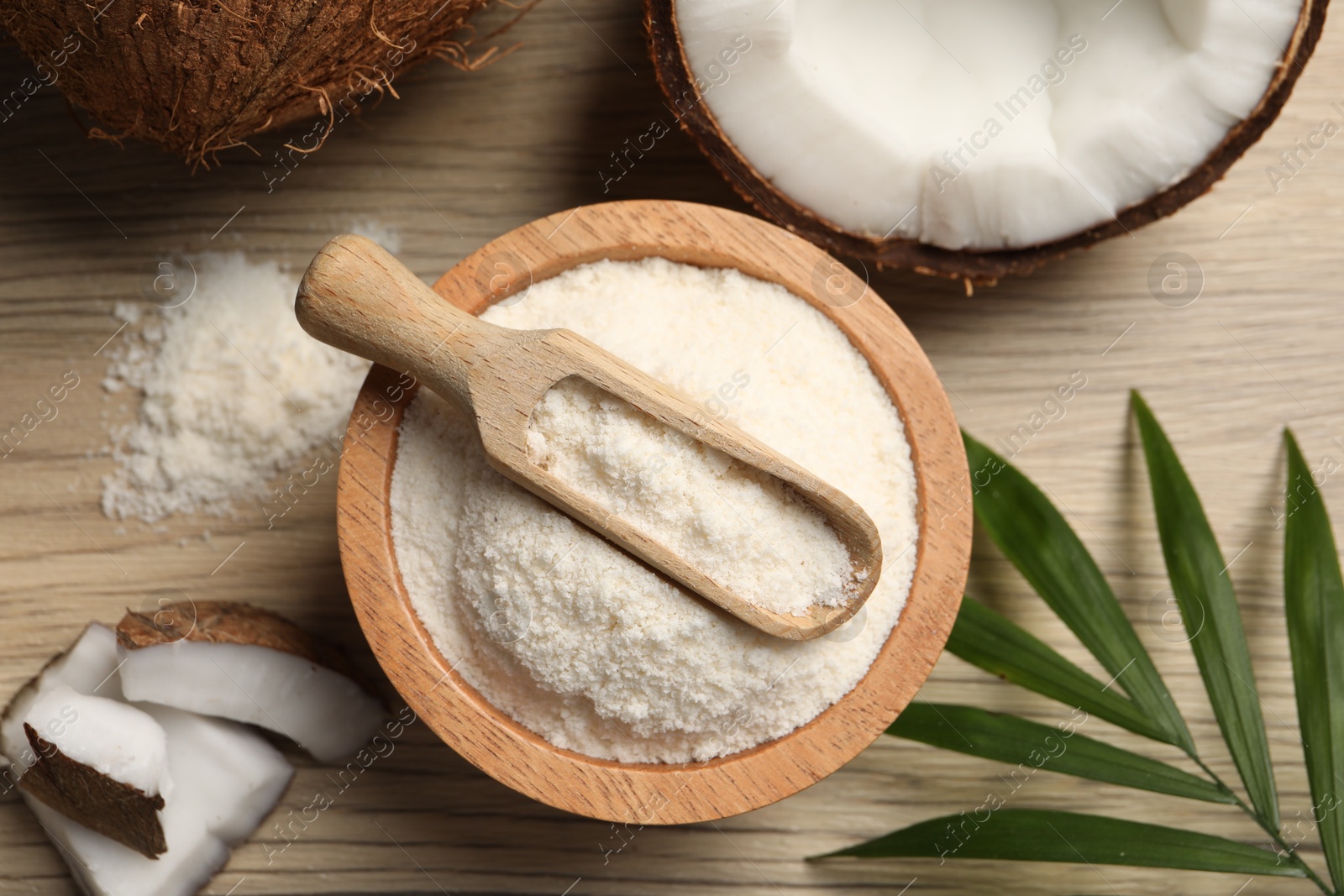 Photo of Fresh coconut flour in bowl, scoop, nut and palm leaf on wooden table, flat lay