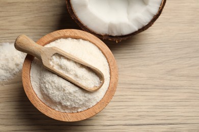 Photo of Fresh coconut flour in bowl, scoop and nut on wooden table, top view. Space for text