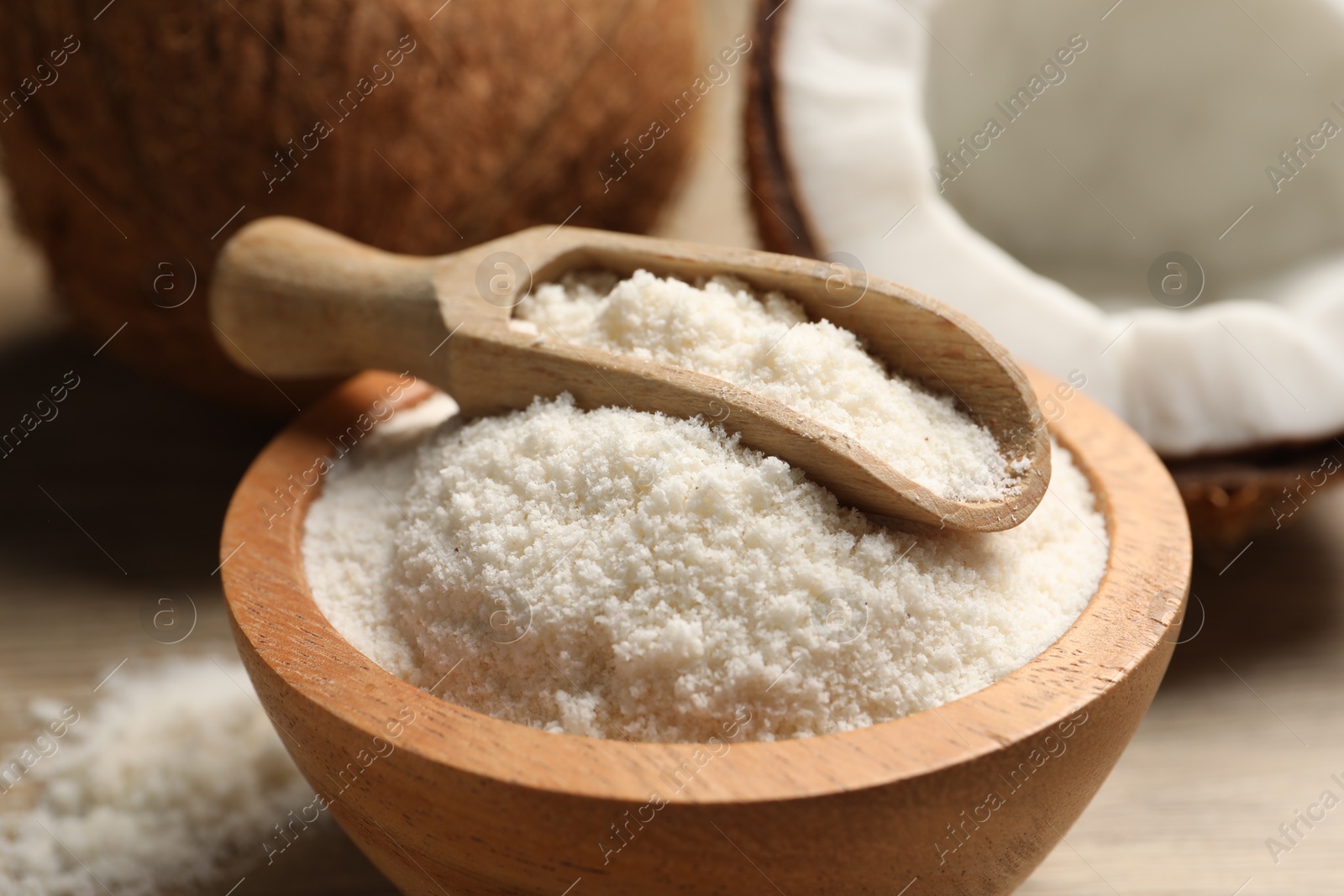 Photo of Fresh coconut flour in bowl, scoop and nut on table, closeup