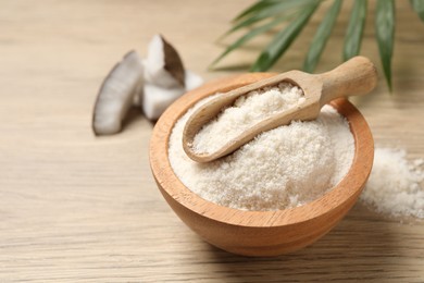 Photo of Fresh coconut flour in bowl, scoop, palm leaf and nut on wooden table