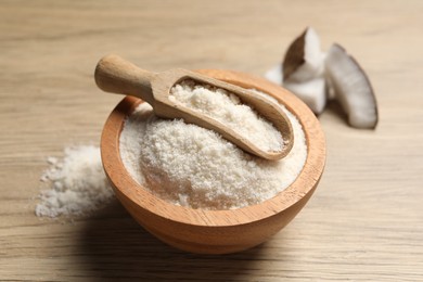 Photo of Fresh coconut flour in bowl, scoop and nut on wooden table