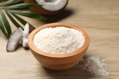 Photo of Fresh coconut flour in bowl, nut and palm leaf on white wooden table