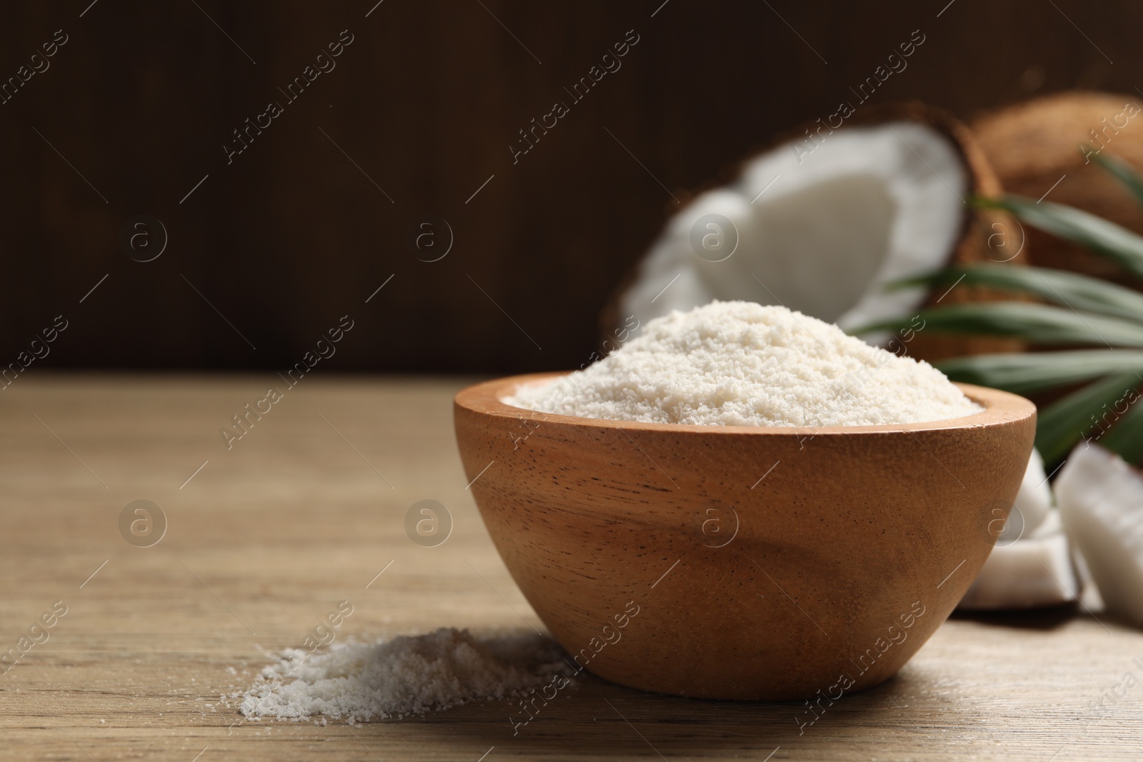 Photo of Fresh coconut flour in bowl, nut and palm leaf on wooden table, space for text