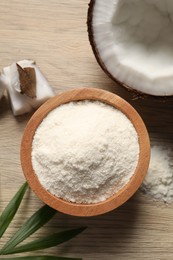 Photo of Fresh coconut flour in bowl, nut and palm leaf on wooden table, flat lay