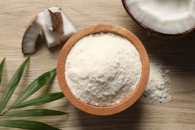 Photo of Fresh coconut flour in bowl, nut and palm leaf on wooden table, flat lay