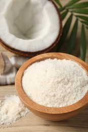 Photo of Fresh coconut flour in bowl, nut and palm leaf on white wooden table