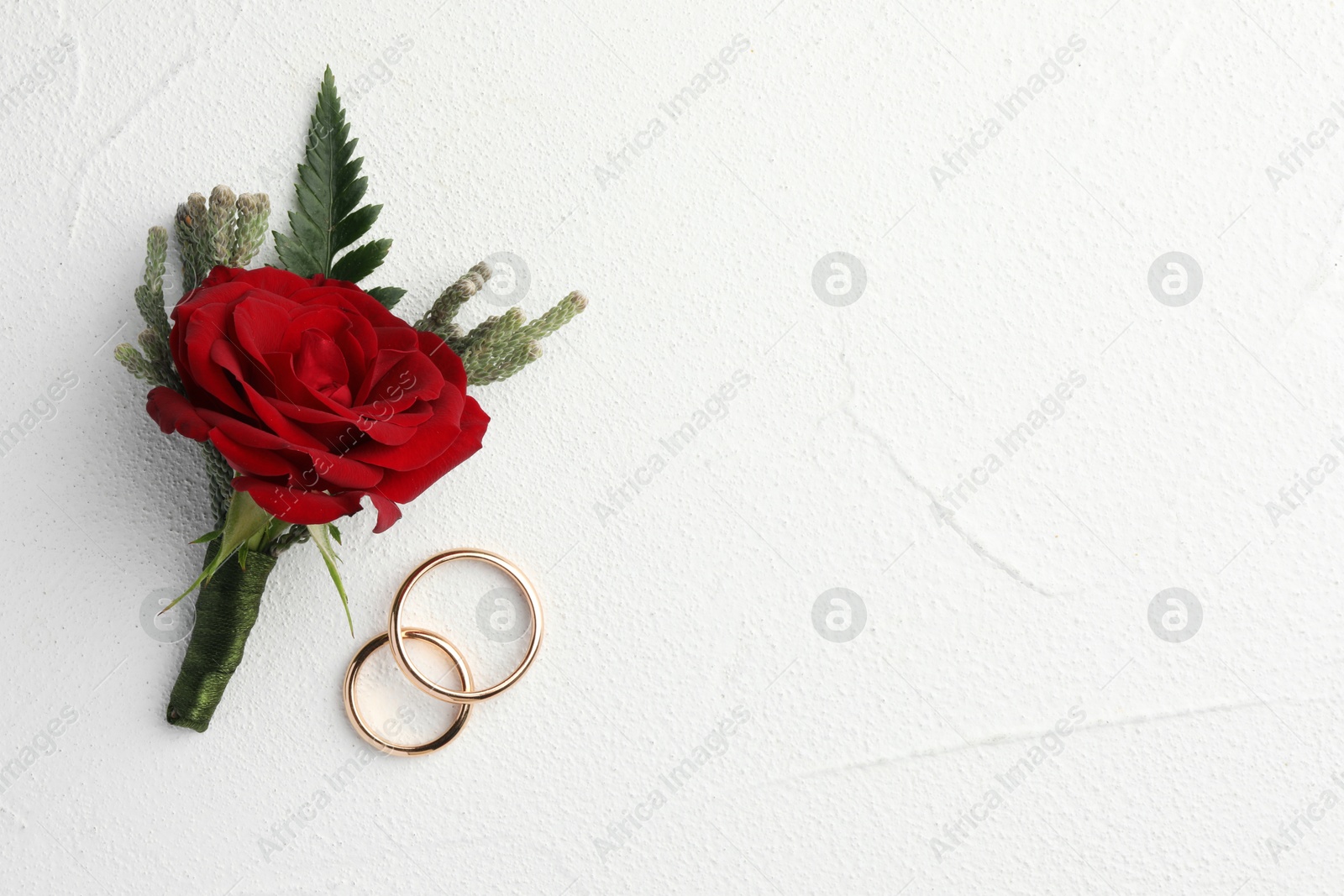 Photo of Stylish red boutonniere and rings on white textured table, top view. Space for text