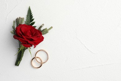 Photo of Stylish red boutonniere and rings on white textured table, top view. Space for text