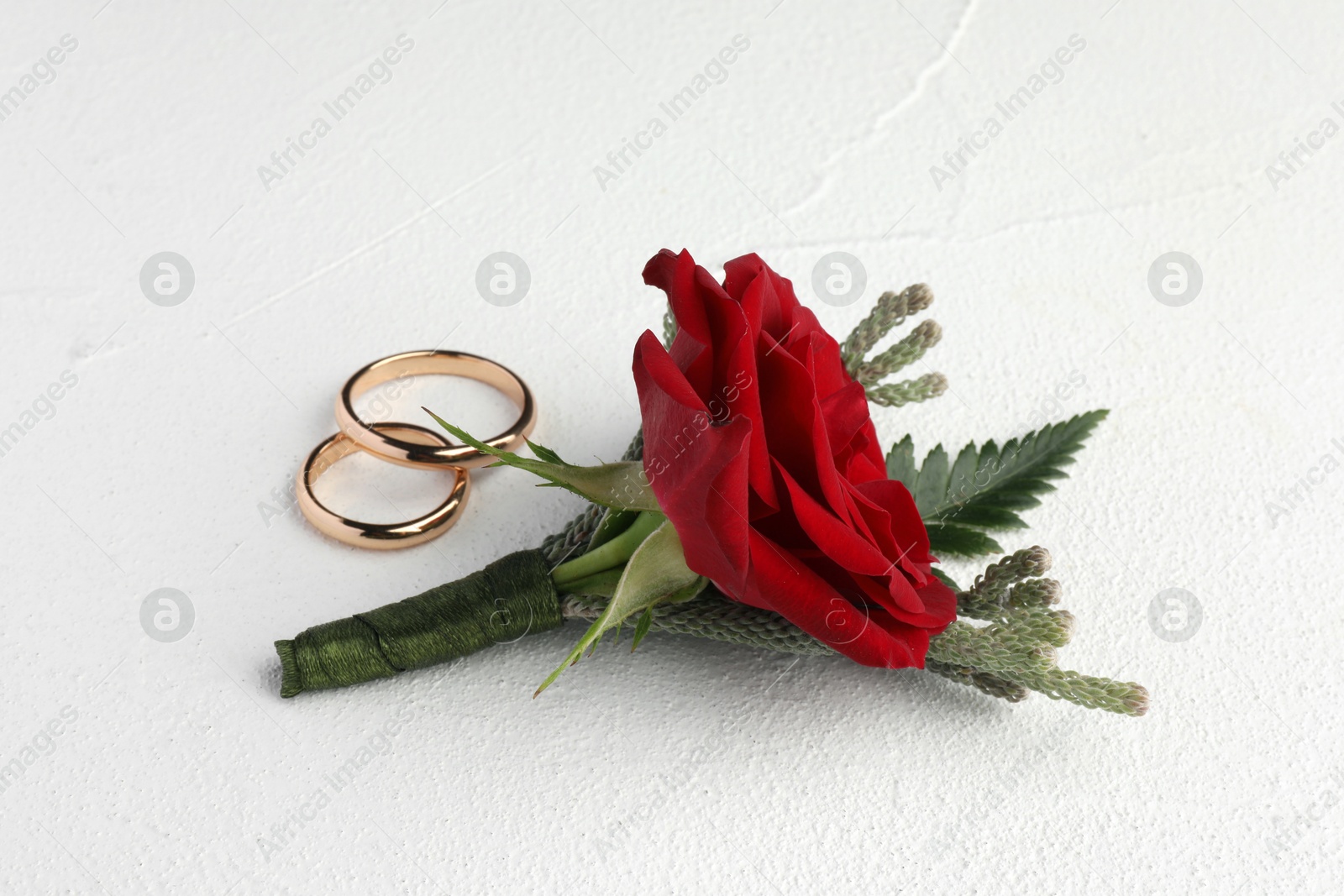 Photo of Stylish red boutonniere and rings on white textured table